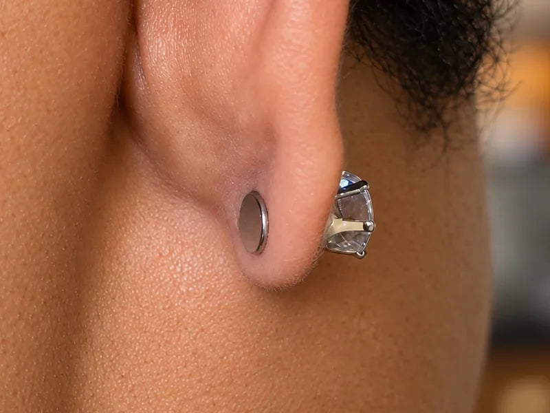 Close-up of the back of an ear wearing a traditional magnetic earring, with a flat magnetic disc behind the earlobe.